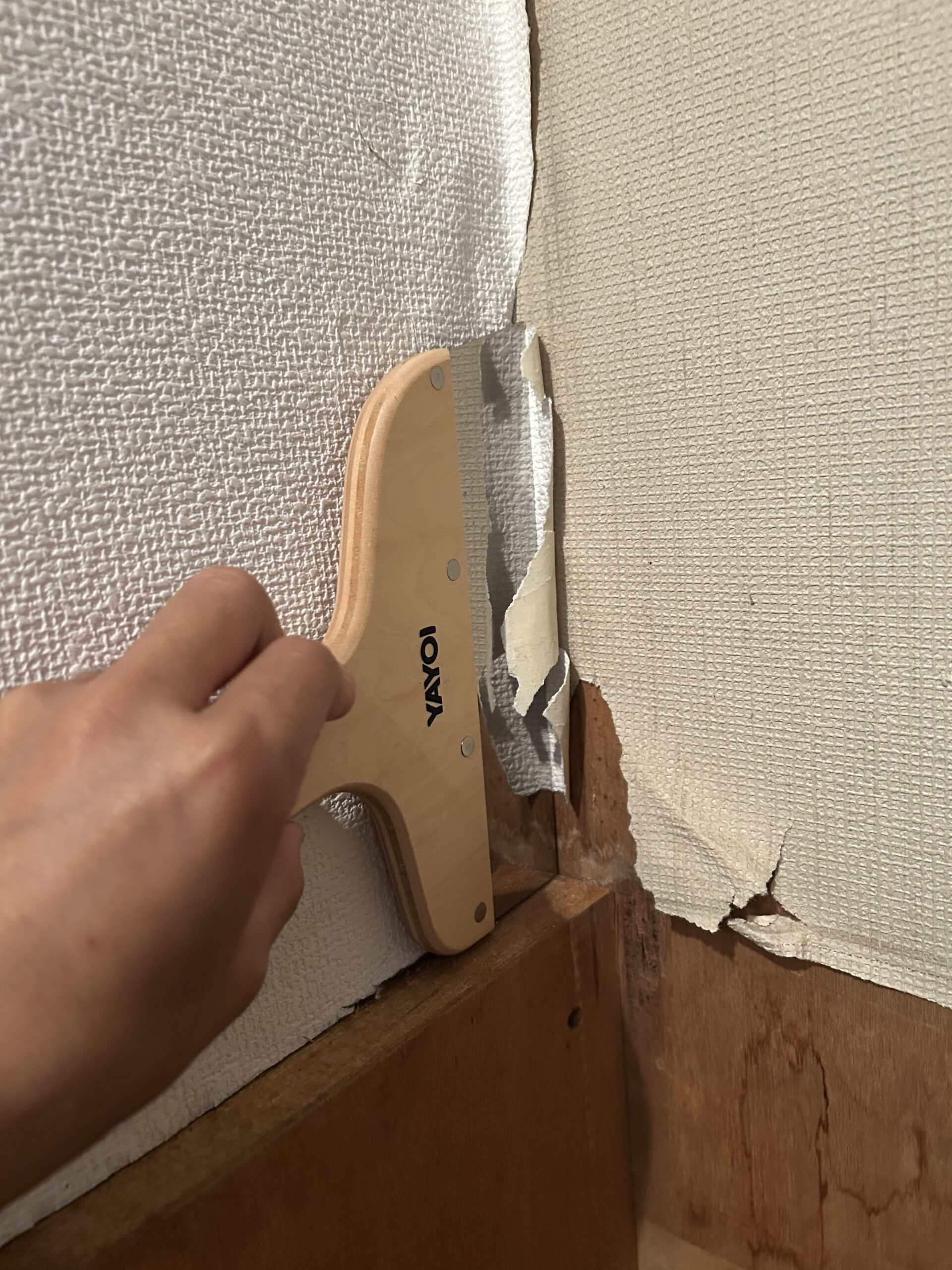 地ベラとカッターで剥がれた壁紙の不要部分を切り取る
