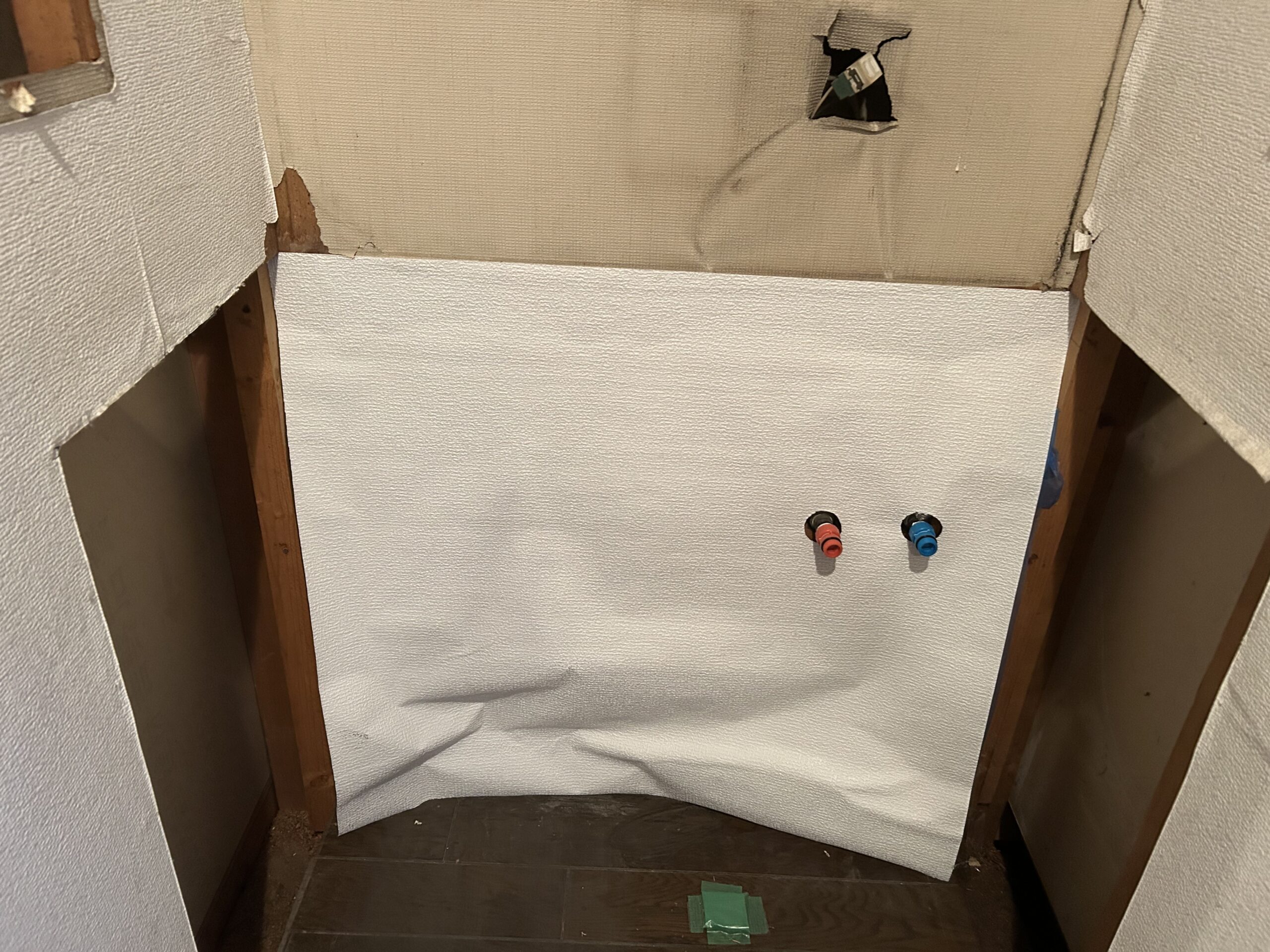 下部の壁にのり付き壁紙を貼る。給水管が出るように穴を開けて貼る
